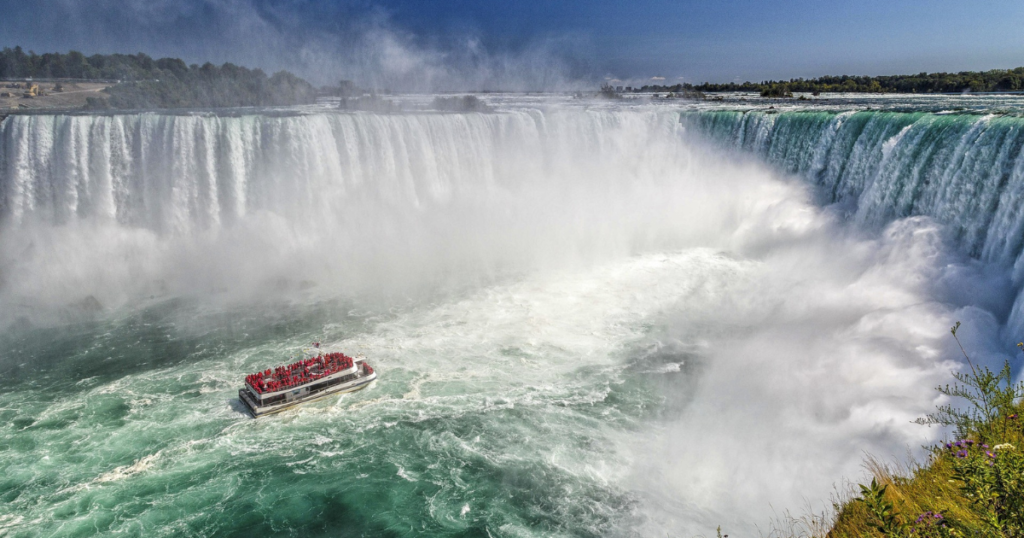 Picture of niagrafalls in canada. in the middle of the falls is a tourist boat and you can see people and travellers on it. 