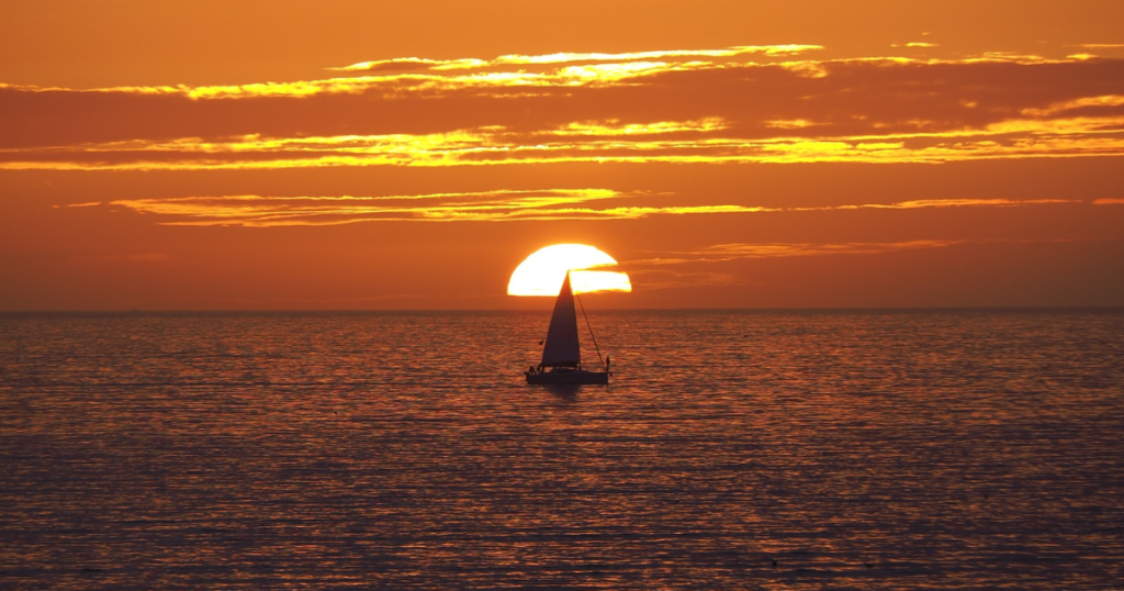 amazing view of sunset over the sea and a sailor boat is just infront of the orange sun 