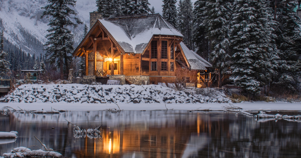 wooden cozy house covered by snow next to a lake. romantic scenery. serves as a picture for gift idea for valetinesday, romantic gift for a traveler, a sweet escape