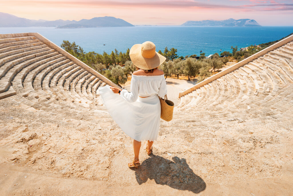 Woman in white dress and hat explores ancient landmark and ruins of Greek amphitheater on coast of the Mediterranean Sea, best personalized travel companies for custom itineraries