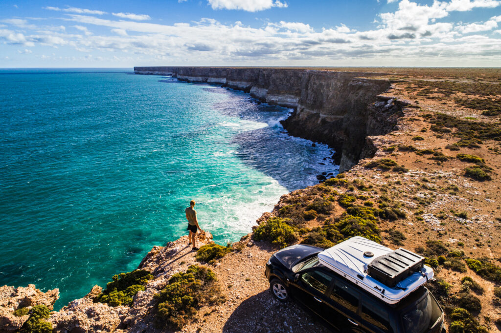 Aerial view a car parked with a camper and a man looking at the cliffs, in Australia.