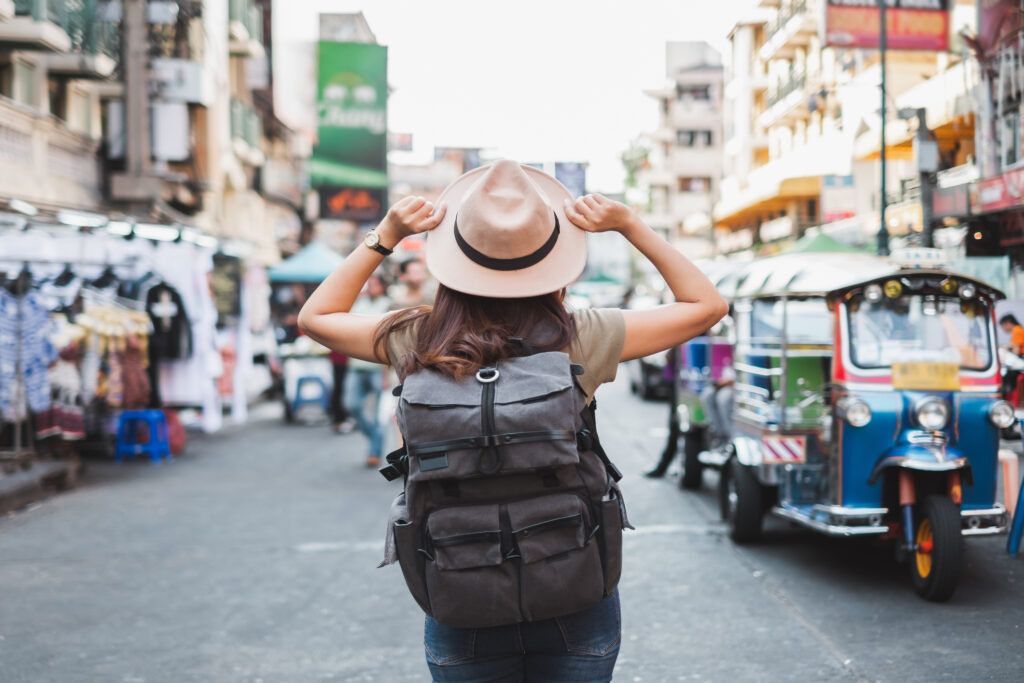 Woman from the back with a hat and a backpack, in the middle of a street in Bangkok, Thailand